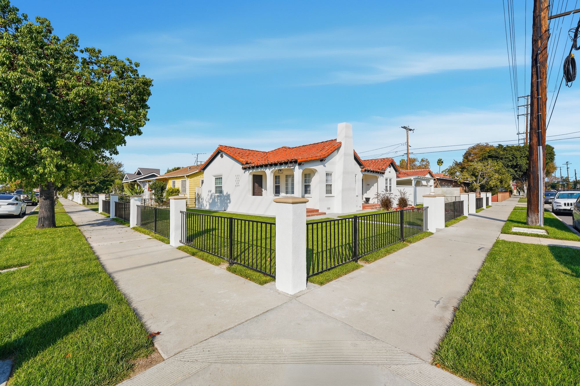 Spanish-style home with a red tile roof and iron fence on a tree-lined street